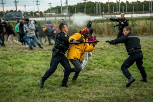 French gendarmes try to stop migrants on the Eurotunnel site in Coquelles near Calais, northern France, on late July 29, 2015. One man died Wednesday in a desperate attempt to reach England via the Channel Tunnel as overwhelmed authorities fought off hundreds of migrants, prompting France to beef up its police presence. AFP PHOTO / PHILIPPE HUGUEN